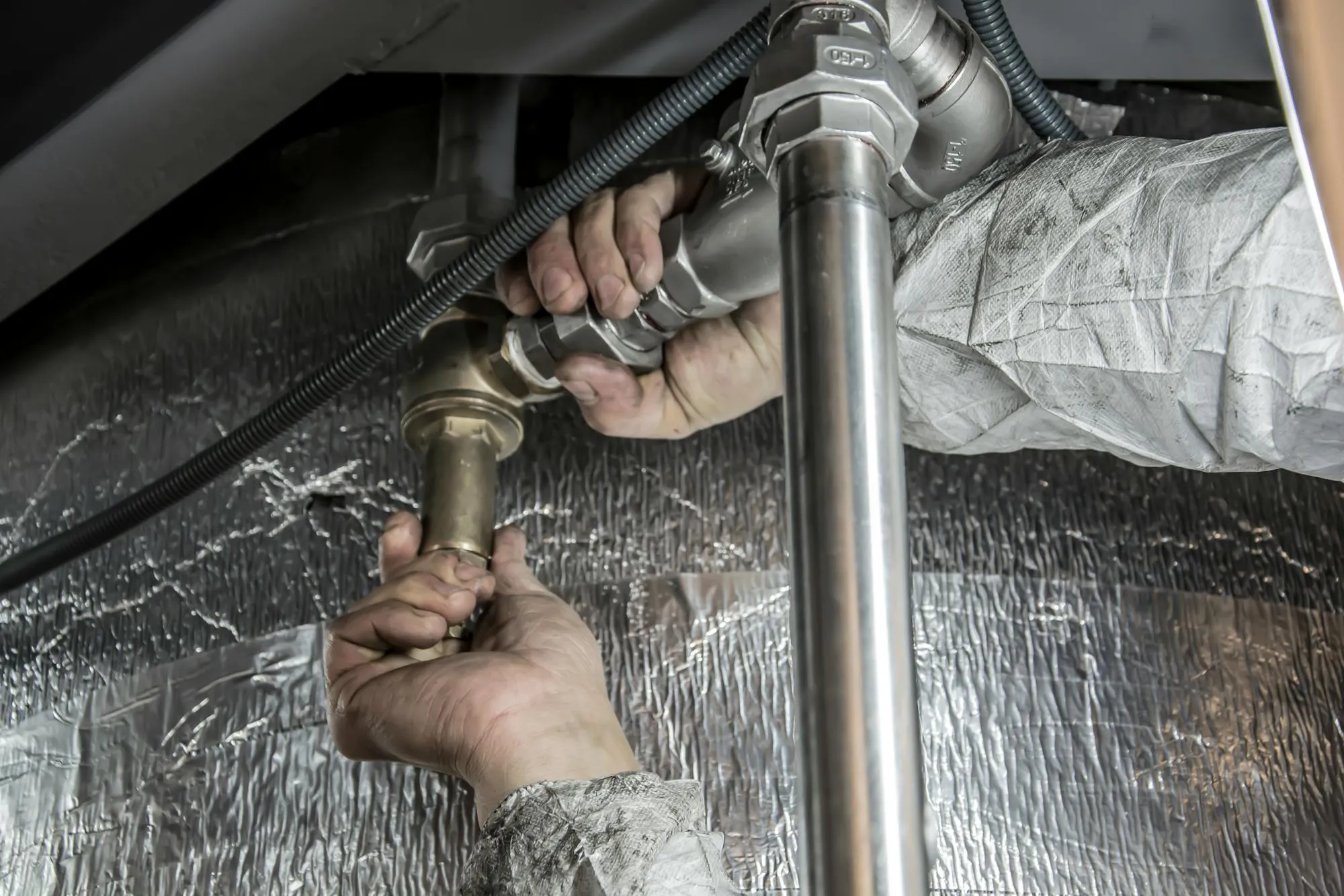 Plumber tightening brass pipe fittings under a sink in an Islington flat